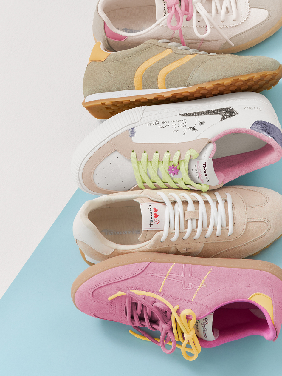 Vari sneaker in colori pastello come rosa, beige e grigio con lacci colorati disposti su uno sfondo azzurro.