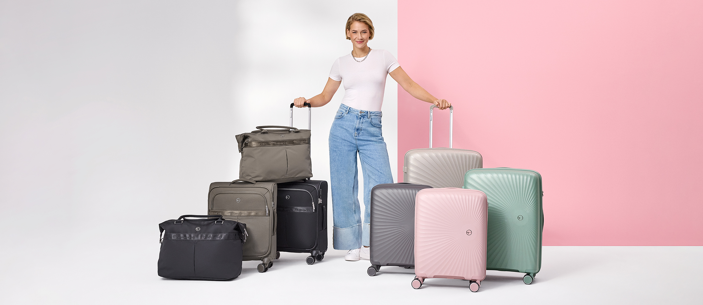 Donna in piedi tra valigie e borse in rosa, verde, grigio e nero su sfondo rosa e bianco.