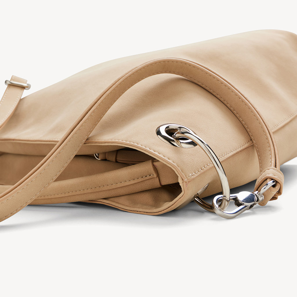 Beige Handtasche mit silbernem Karabinerhaken und Tragegriff, Nahaufnahme auf hellem Hintergrund.