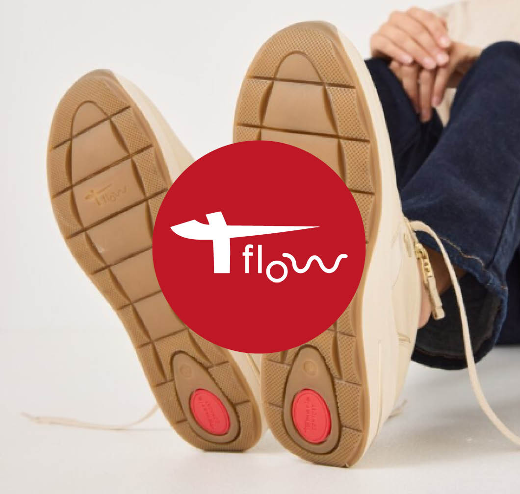 Person sitting with legs raised, showing the soles of beige trainers, with a red T‑Flow logo in the foreground.