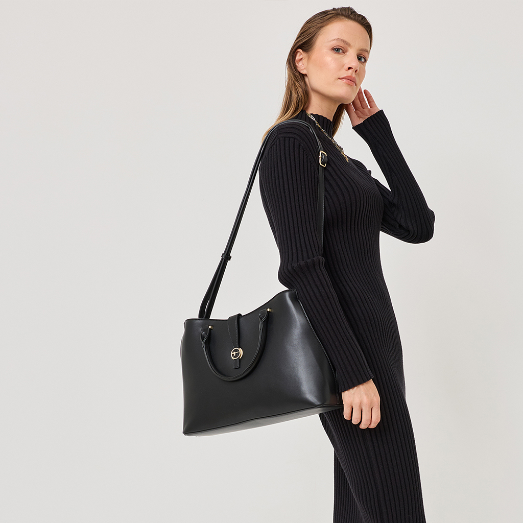 Elegante zwarte gebreide jurk met een col en een zwarte leren handtas met gouden details tegen een witte achtergrond.