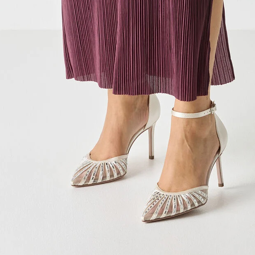 Elegante cr&egrave;mekleurige high heels met een stralenpatroon op de punt, gecombineerd met een geplooide bordeauxrode rok.