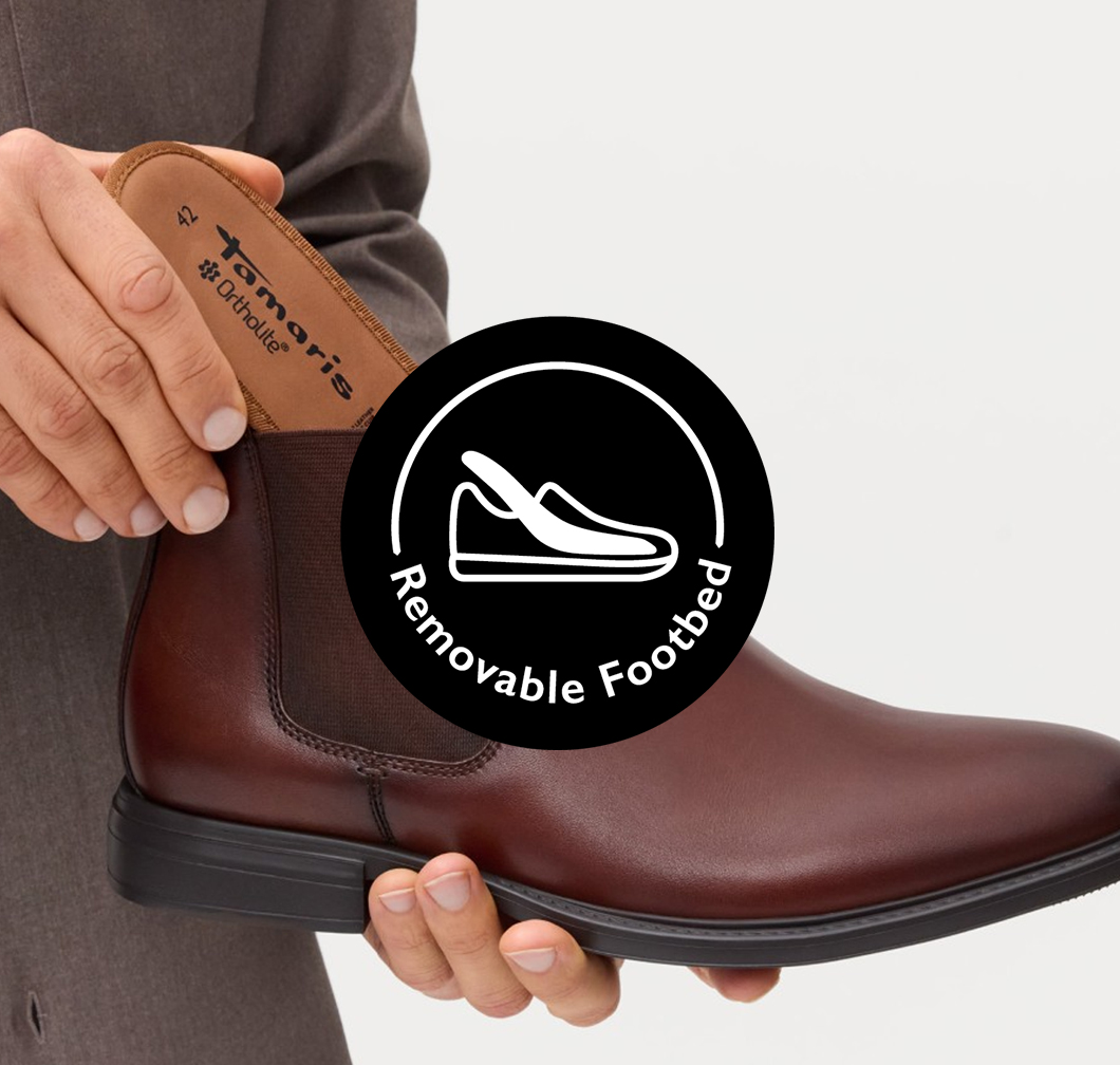 Een persoon haalt de uitneembare inlegzool uit een bruine Tamaris Chelsea-boot. Zwart logo met de tekst "Removable Footbed".