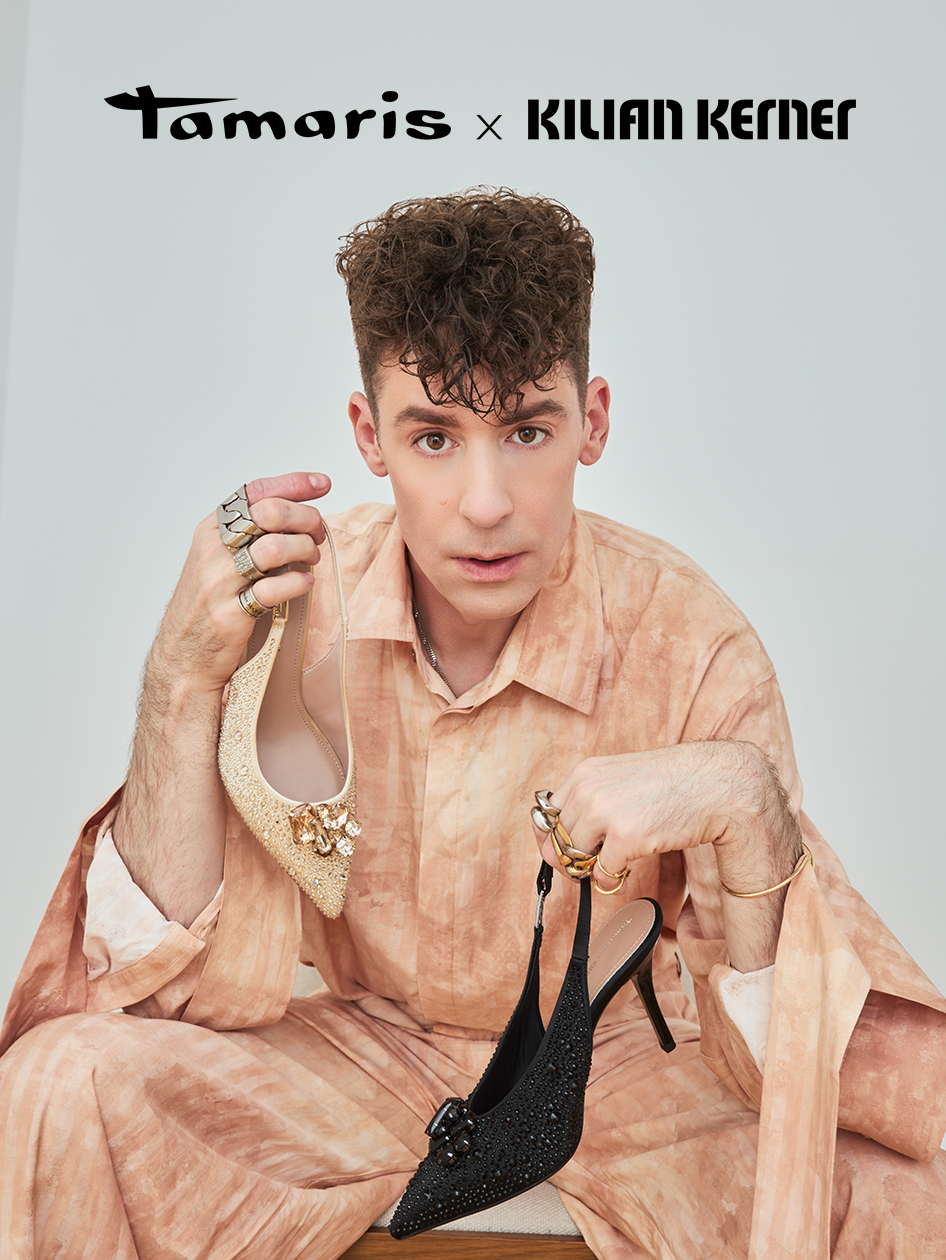Kilian Kerner h&auml;lt zwei Schuhe der Tamaris x Kilian Kerner Kollektion: einen goldenen und einen schwarzen Slingback-Stiletto.