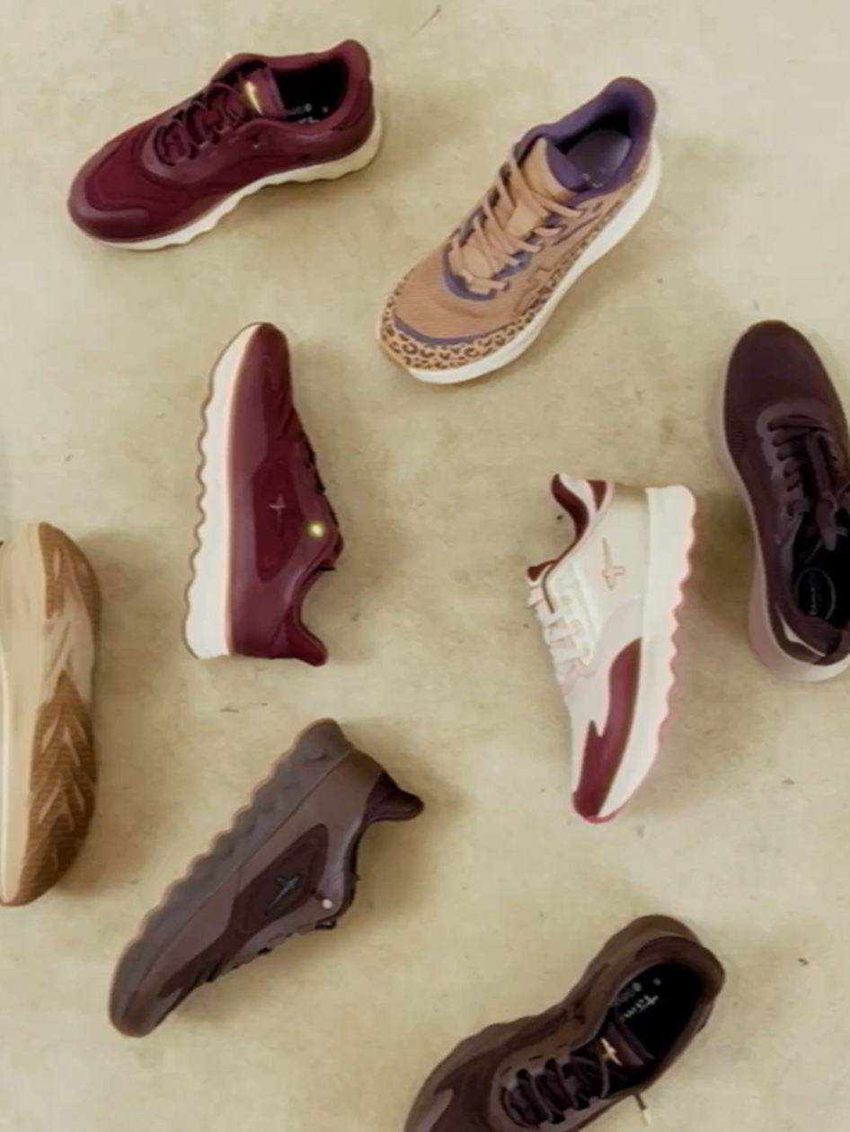 Various sneakers in burgundy, beige, white and brown, including a leopard‑print model, on a light surface.