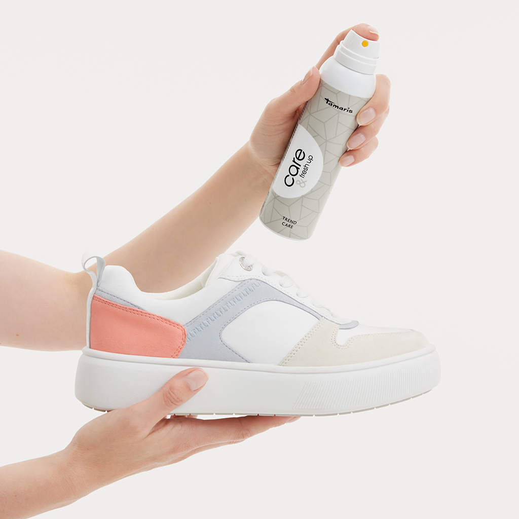 Weißer Sneaker mit rosa und grauen Akzenten wird mit Schuhpflegespray behandelt