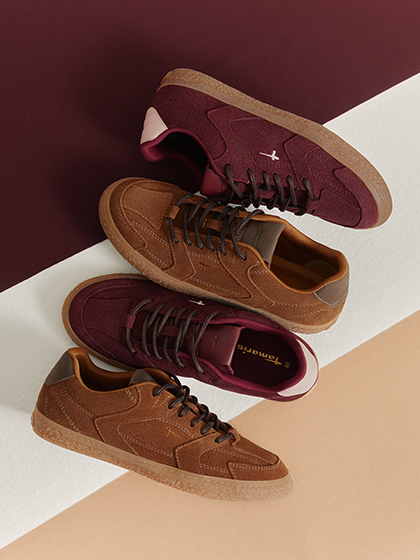 Zwei Tamaris Sneaker in Bordeauxrot und Braun mit Schn&uuml;rsenkeln auf zweifarbigem Hintergrund.