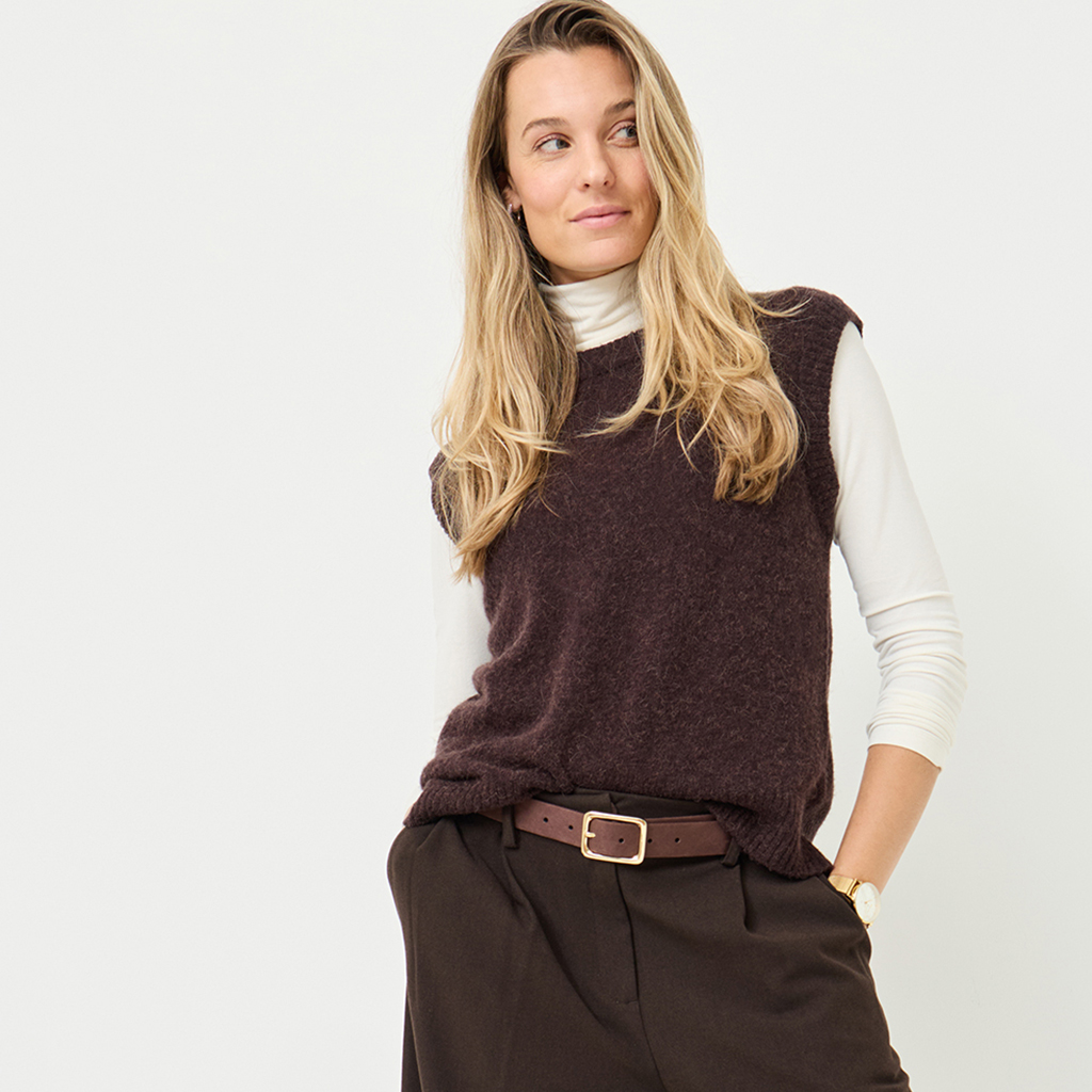 Moderne efterårsoutfit med brun strikvest over hvid rullekravetrøje, brune bukser og læderbælte