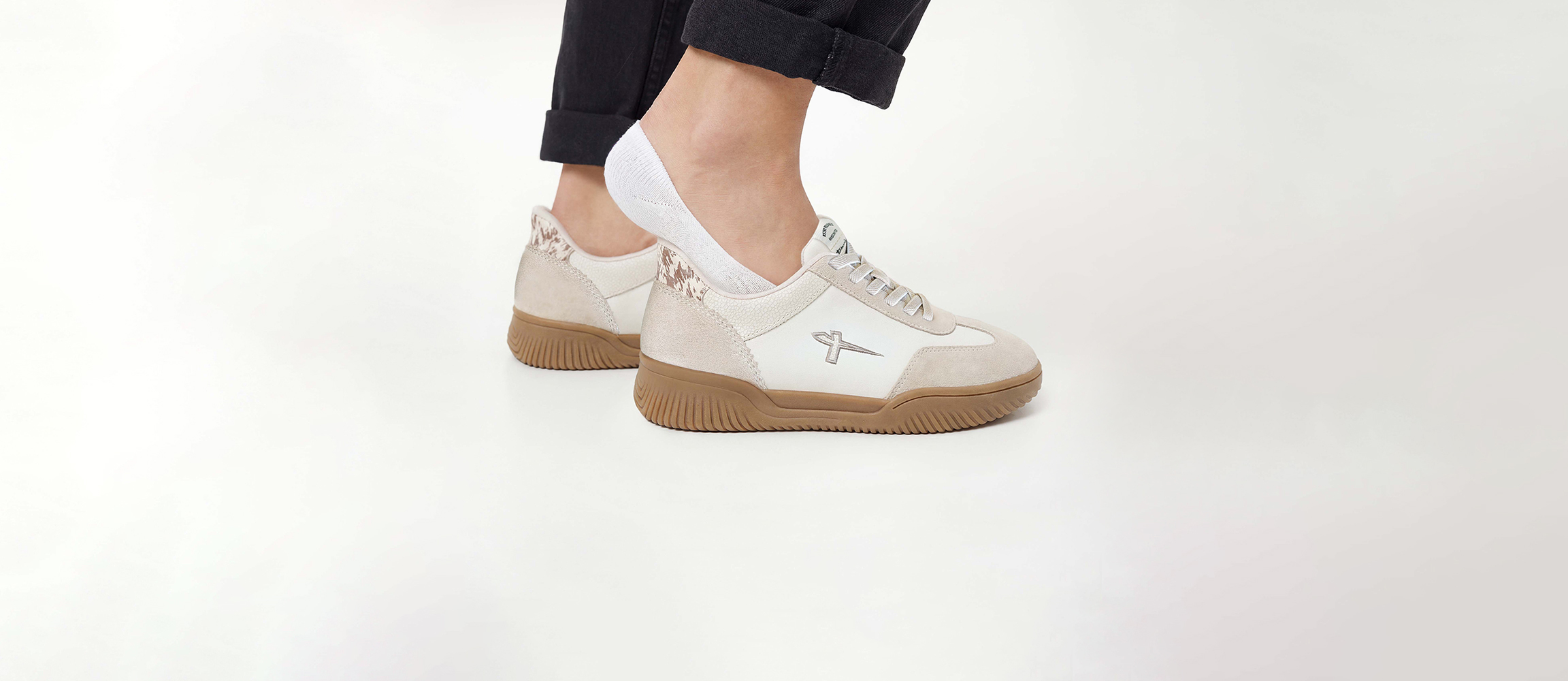 Beige-wei&szlig;e Sneaker mit brauner Gummisohle, getragen mit schwarzer Hose und wei&szlig;en Socken.