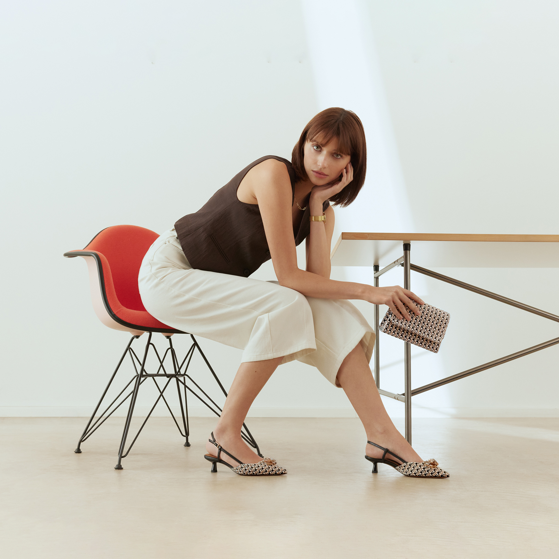 Elegant outfit med sort top, hvide bukser, m&oslash;nstrede slingback-sko og matchende clutch i moderne omgivelser