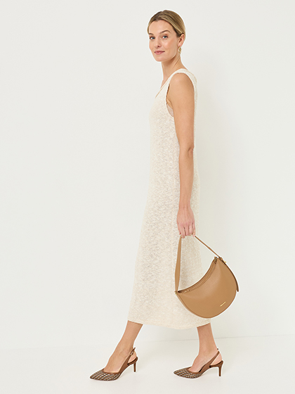 Vrouw in een mouwloze midi-jurk in cr&egrave;mewit met een bruine handtas en geprinte slingback‑pumps.
