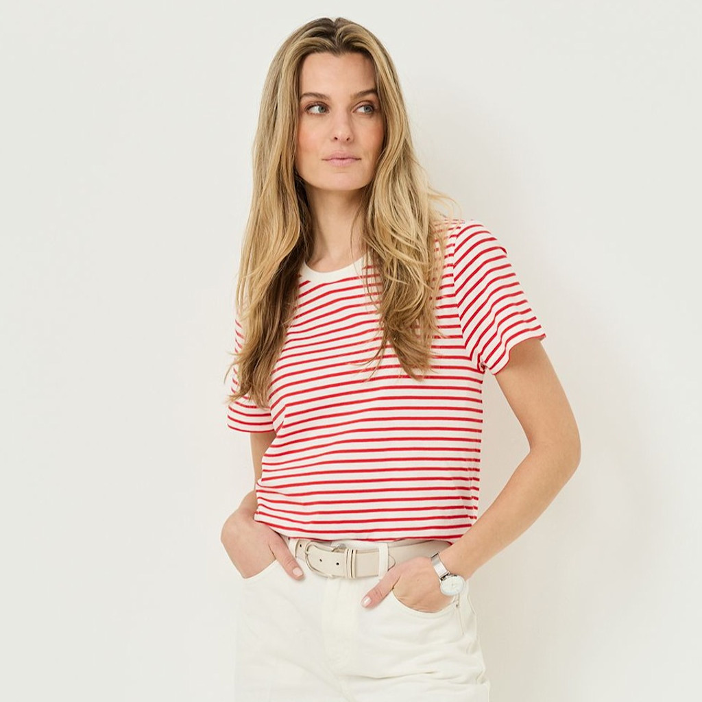 Person in a red-and-white striped T-shirt and white pants poses in a casual stance against a light background.