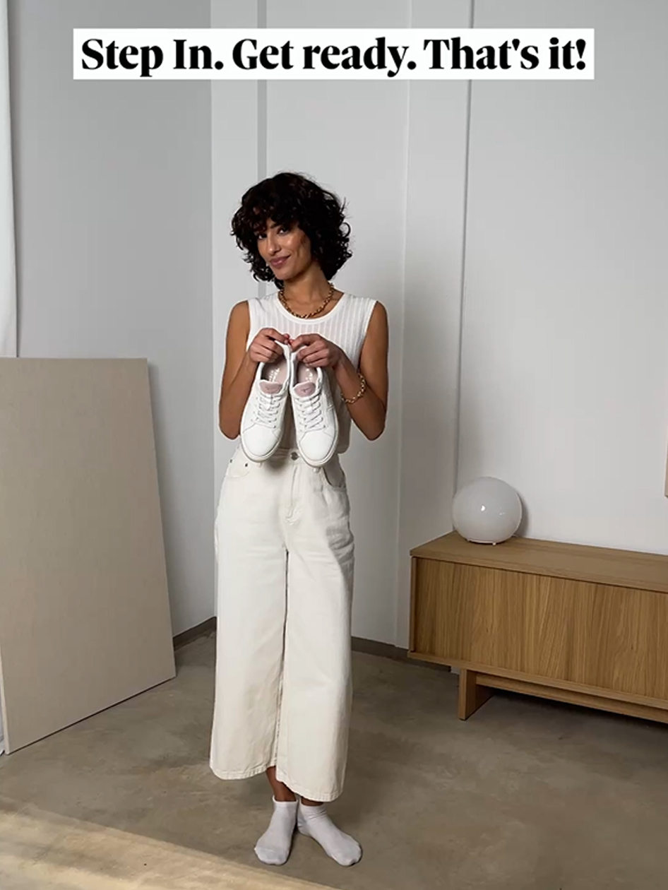 Donna in outfit bianco tiene in mano sneakers bianche.