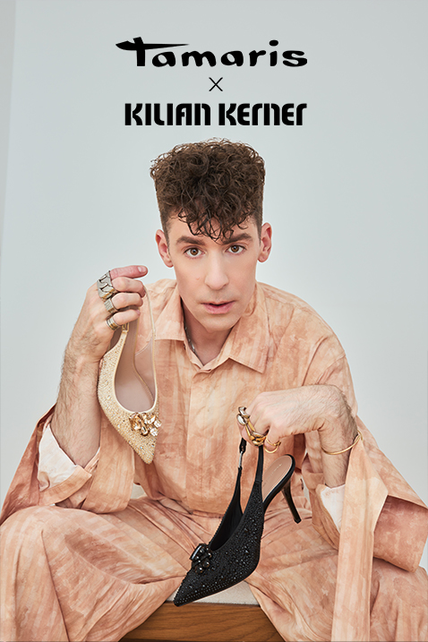 Kilian Kerner is holding two elegant shoes from the Tamaris x Kilian Kerner collection: a gold one and a black high-heeled shoe.