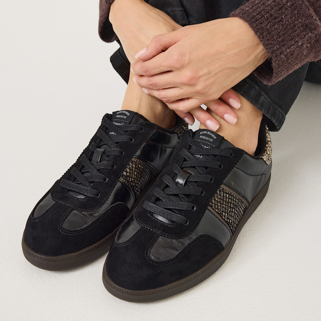 Svarta sneakers med ormskinnsdetaljer och brun sula, burna med m&ouml;rka byxor