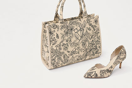 Beige Handtasche und passender Pumps mit schwarzem Blumenmuster, elegantes Set auf wei&szlig;em Hintergrund