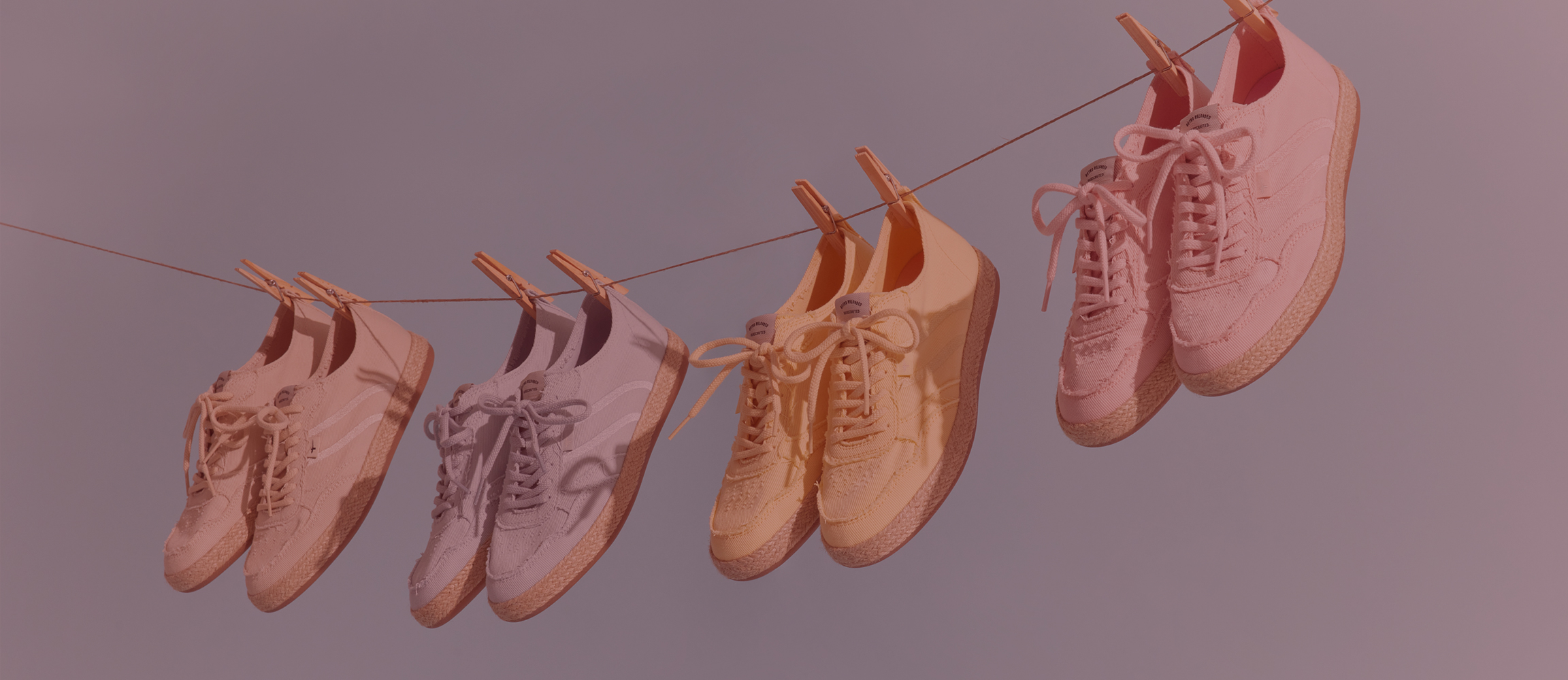 Quattro paia di sneakers in tonalit&agrave; pastello appese a una corda con mollette.
