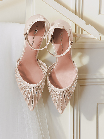 Elegante cr&egrave;mekleurige pumps met kristallen versieringen hangen aan een kledinghanger voor een witte houten muur.