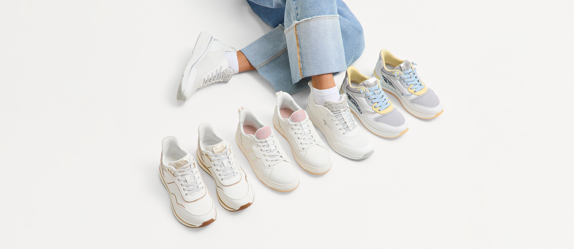 Meerdere witte sneakers in een diagonale rij gerangschikt, met lichtblauwe en gele accenten en een persoon in jeans.