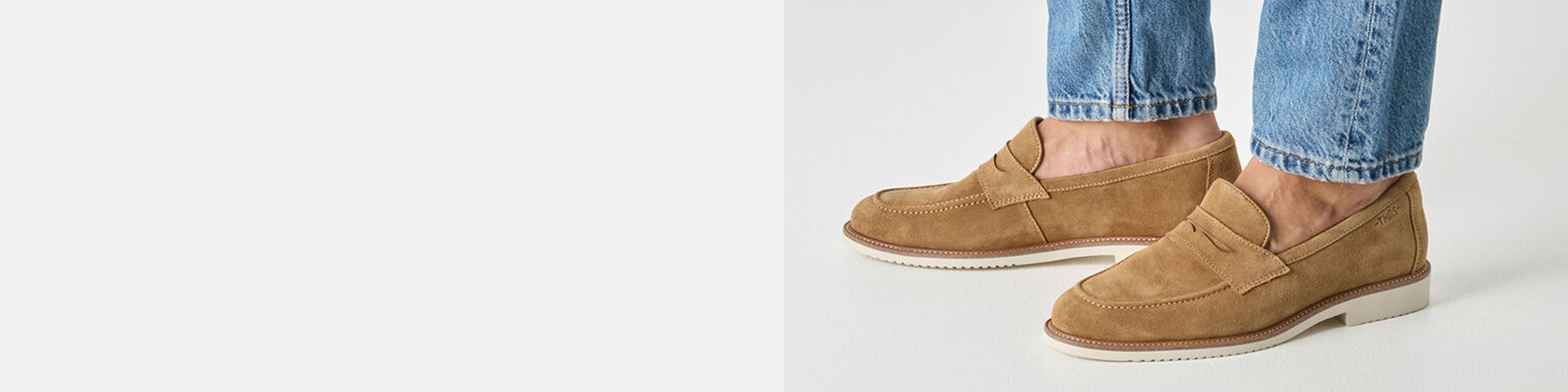 Ben in een blauwe jeans met lichtbruine su&egrave;de loafers met witte zool tegen een lichte achtergrond.