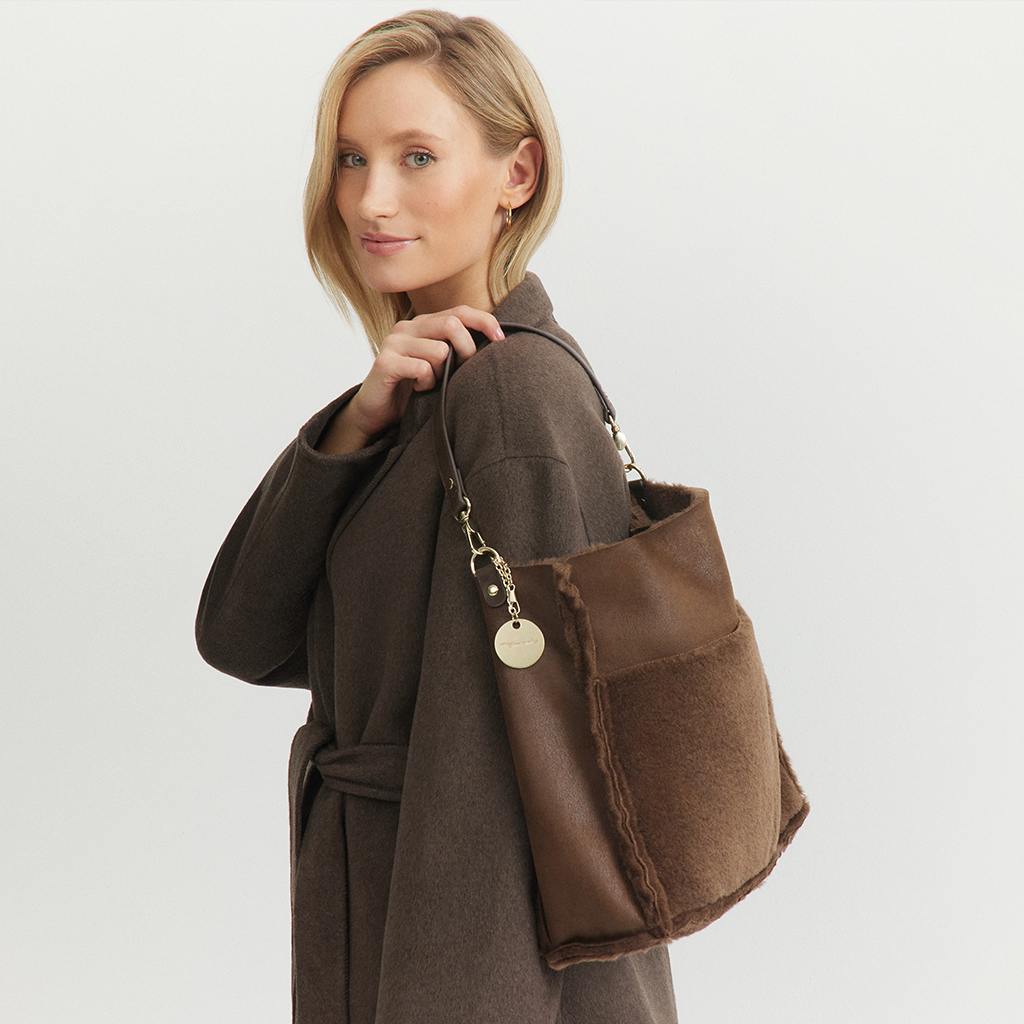 Portrait de mode élégant d'une femme en manteau marron avec un sac à main assorti sur fond blanc.