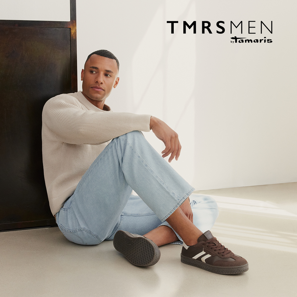 Man sitting on the floor, wearing a beige knitted jumper, light blue jeans and brown trainers by TMRS MEN by Tamaris.