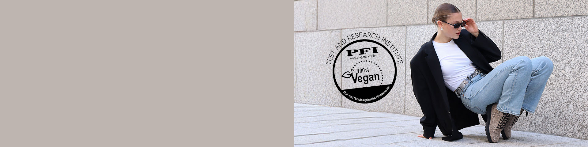 Una persona in abbigliamento streetwear casual è seduta su un muro grigio, indossa jeans e un cappotto nero.