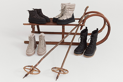 Various winter boots and snowshoes in black and white, lined up on a sled.