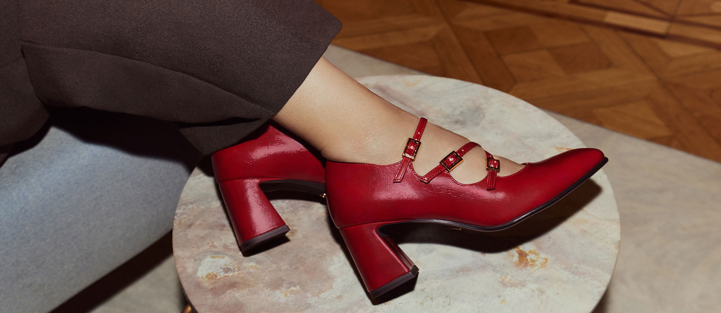Rote Lacklederschuhe mit drei Riemen und hohem Blockabsatz auf marmorierter Oberfläche.