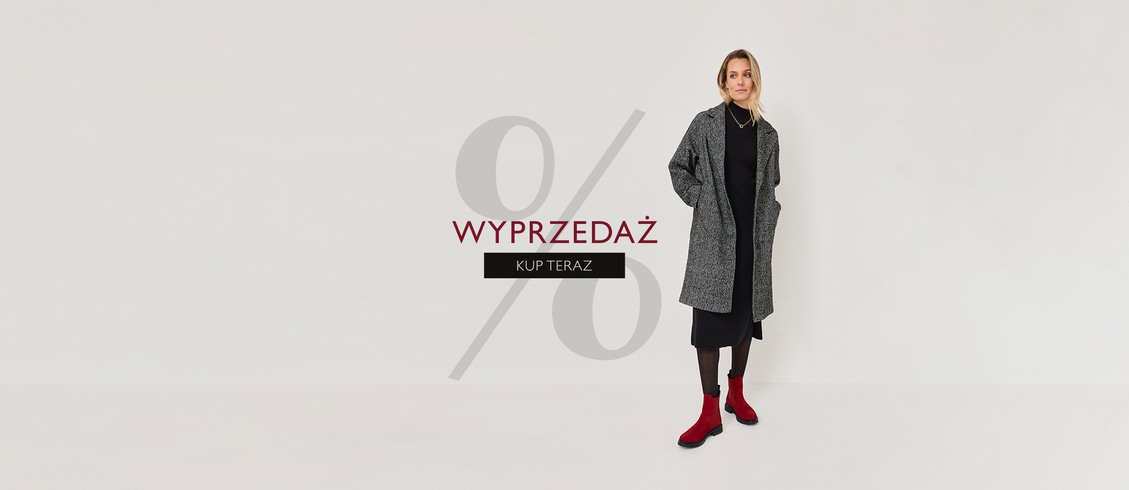 Reklama mody z procentem: Osoba w szarym płaszczu, czarnej sukience i czerwonych butach na białym tle.
