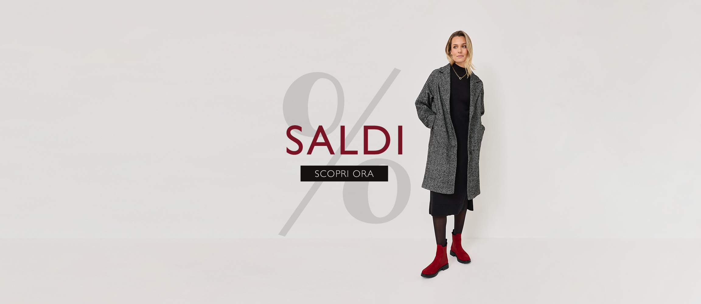 Pubblicit&agrave; di moda con segno percentuale: Persona in cappotto grigio, abito nero e stivali rossi su sfondo bianco.