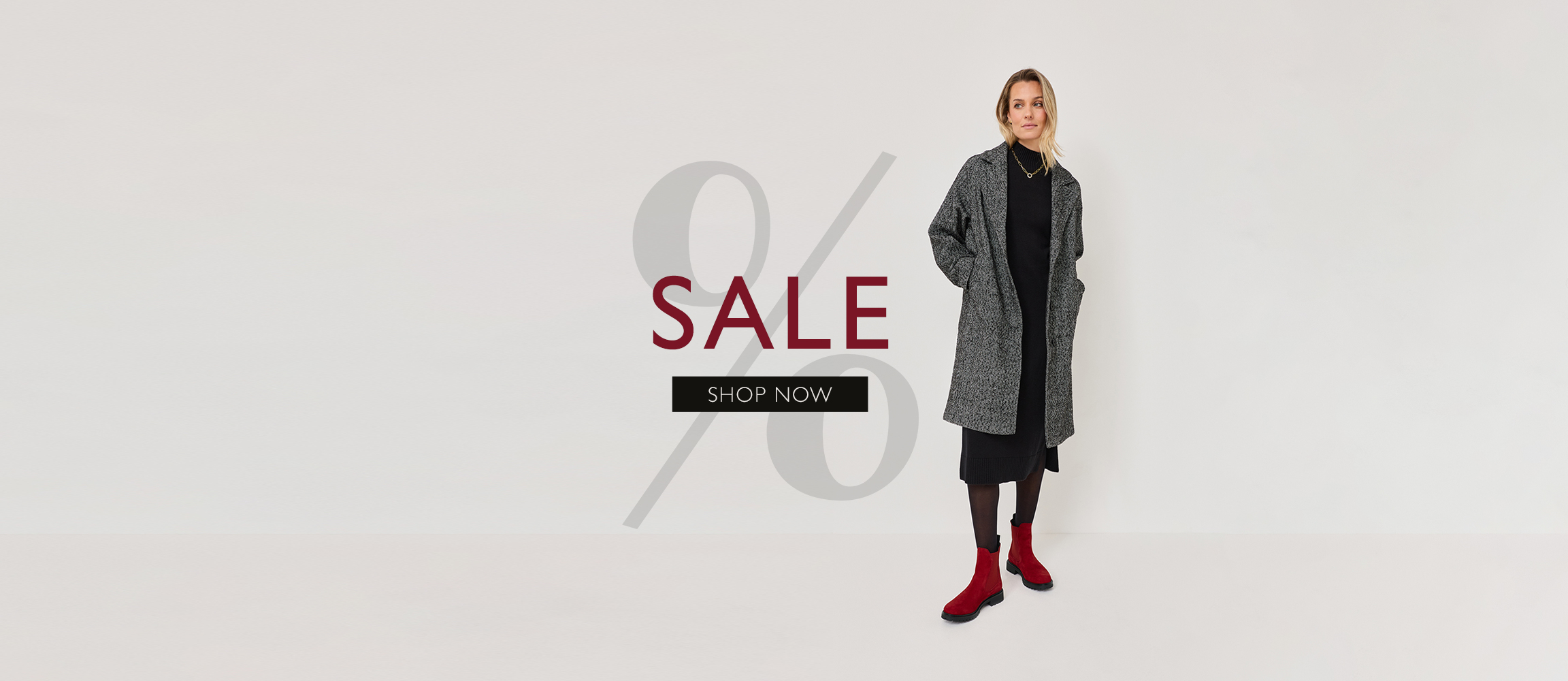 Percentage sign fashion advertisement: person in grey coat, black dress and red boots against a white background.