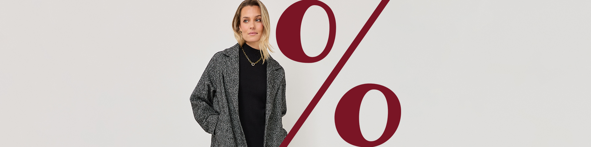 Frau in grauem Blazer und schwarzem Top vor b&iacute;l&yacute;m pozad&iacute;m s v&iacute;nově červen&yacute;m procentn&iacute;m znakem