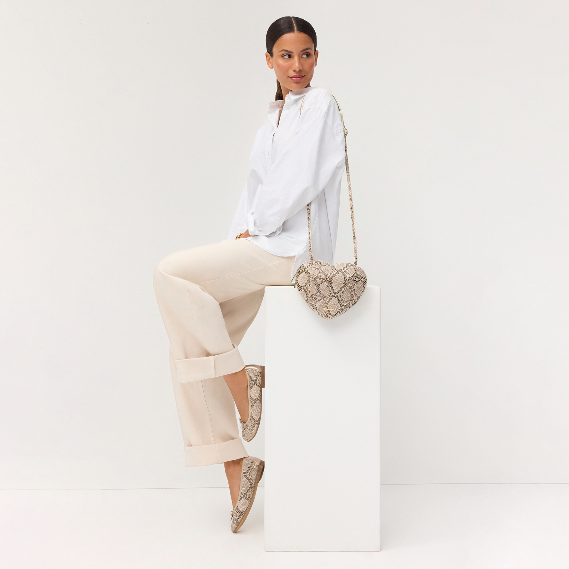 Trendigt outfit med vit blus, beige byxor och skor i ormm&ouml;nstrad look, kompletterad med matchande v&auml;ska mot vit bakgrund.