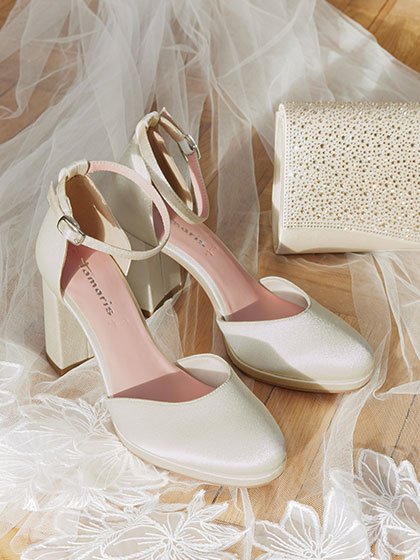 Elegante witte bruidsschoenen en clutch&shy;tassen op een houten vloer, omringd door fijne tule.