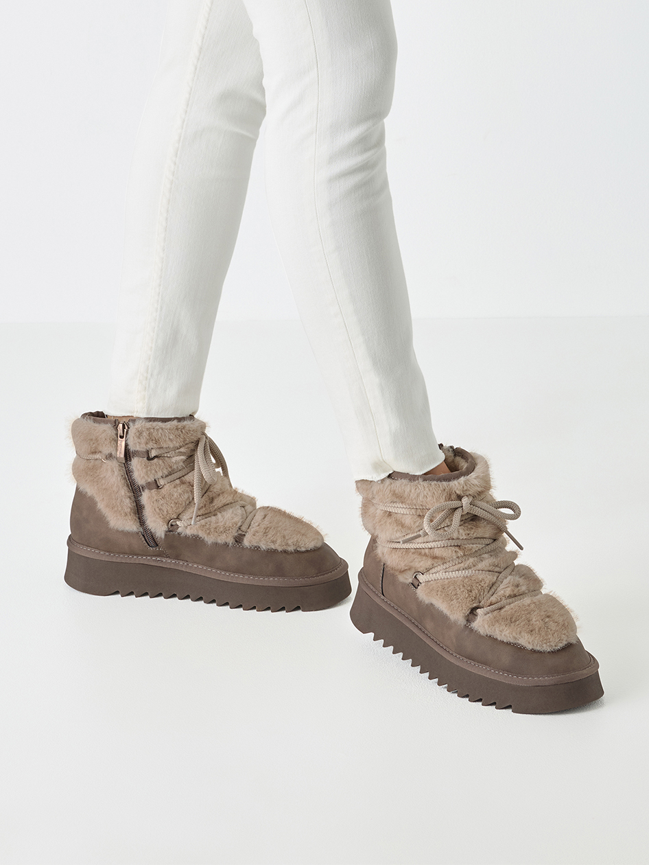 Bottes d'hiver chaudes en taupe avec fourrure duveteuse, lacets et semelle compensée robuste, portées avec un pantalon blanc.