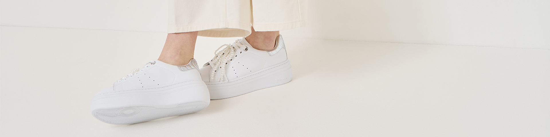 Hvide plateau-sneakers med s&oslash;lvfarvede detaljer og perledekoration, stylet med cremefarvede bukser.