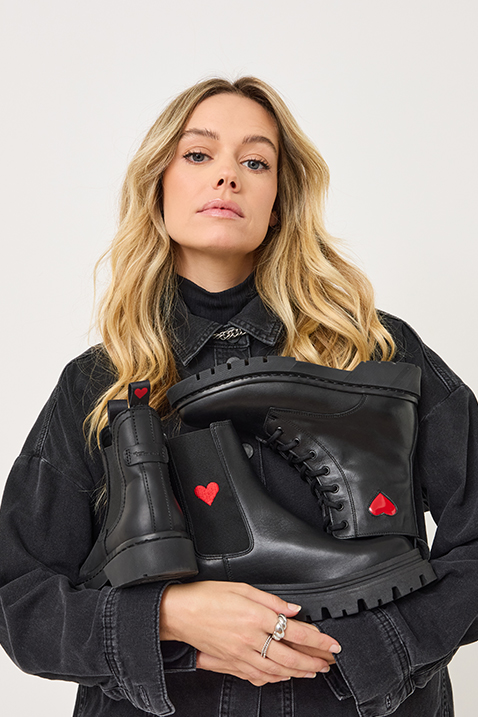 Woman with black denim jacket and black boots with red heart details, on a light background