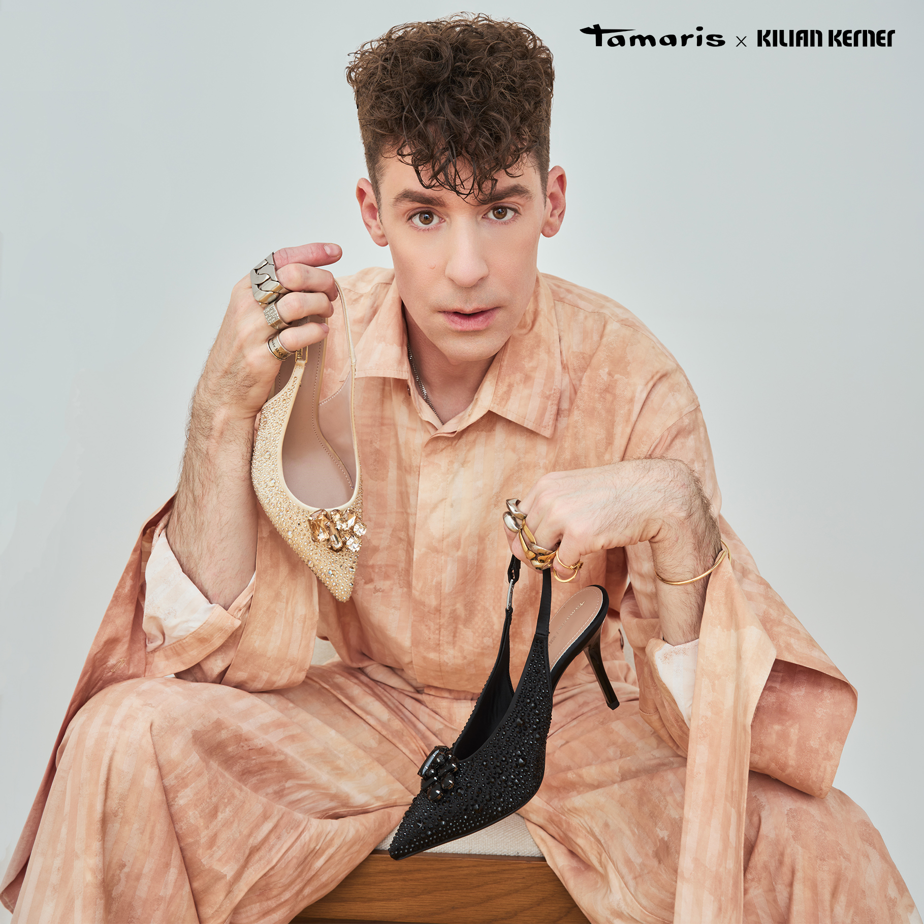 Person h&auml;lt goldenen und schwarzen High Heel, mit Schriftzug "Kilian Kerner" im Hintergrund.