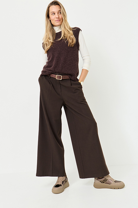 The model is wearing a brown sweater over a white turtleneck, brown Palazzo trousers with a belt and beige sneakers against a white background.