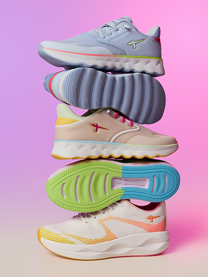 Des chaussures de sport color&eacute;es dans des tons pastels flottent sur fond rose, empil&eacute;es dans une composition dynamique.