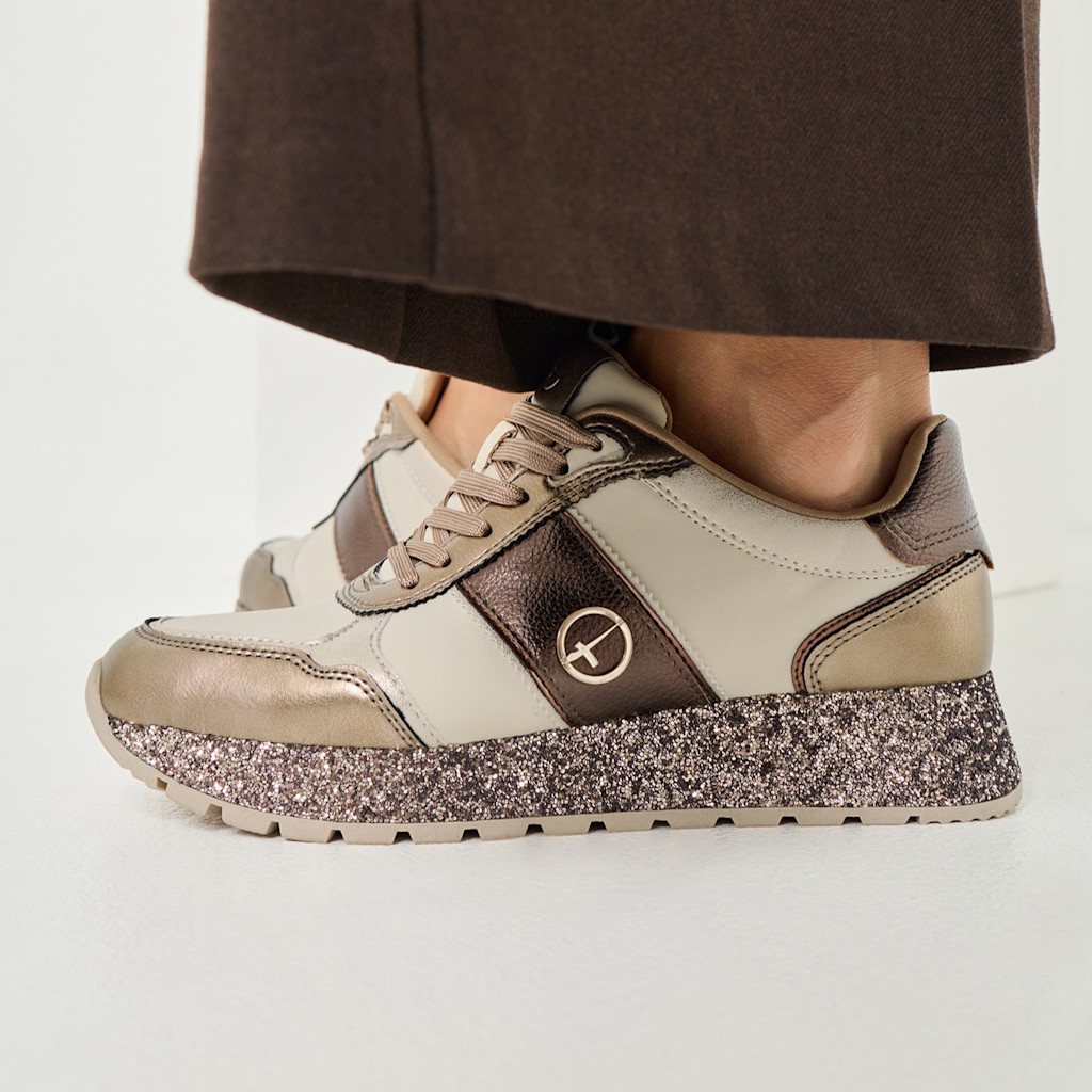 Basket sportive en Beige et Bronze avec semelle plateforme scintillante, portée avec un pantalon foncé.