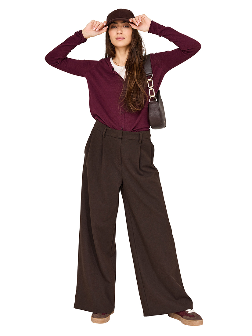 Modisches Herbstoutfit mit weinrotem Cardigan, weiter brauner Hose, Baseballkappe und Handtasche in eleganter Casual-Pose