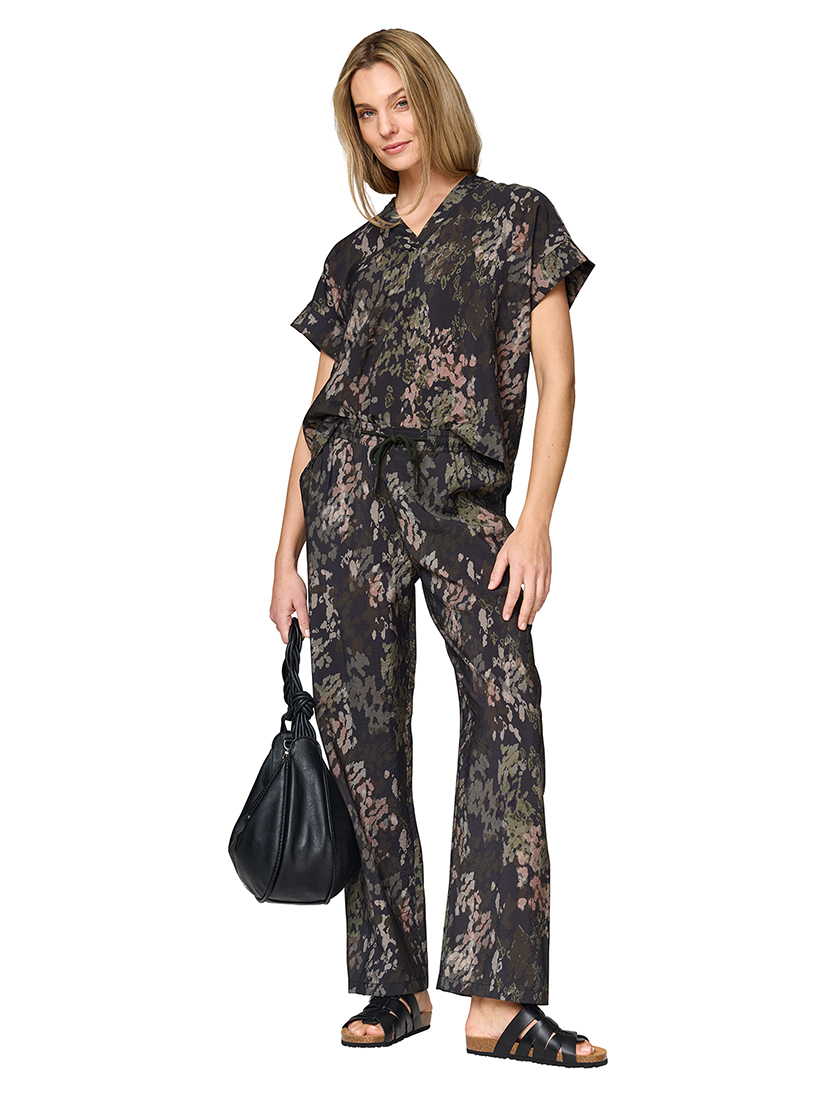 Woman in a dark green two-piece floral outfit with a black handbag and black mules.