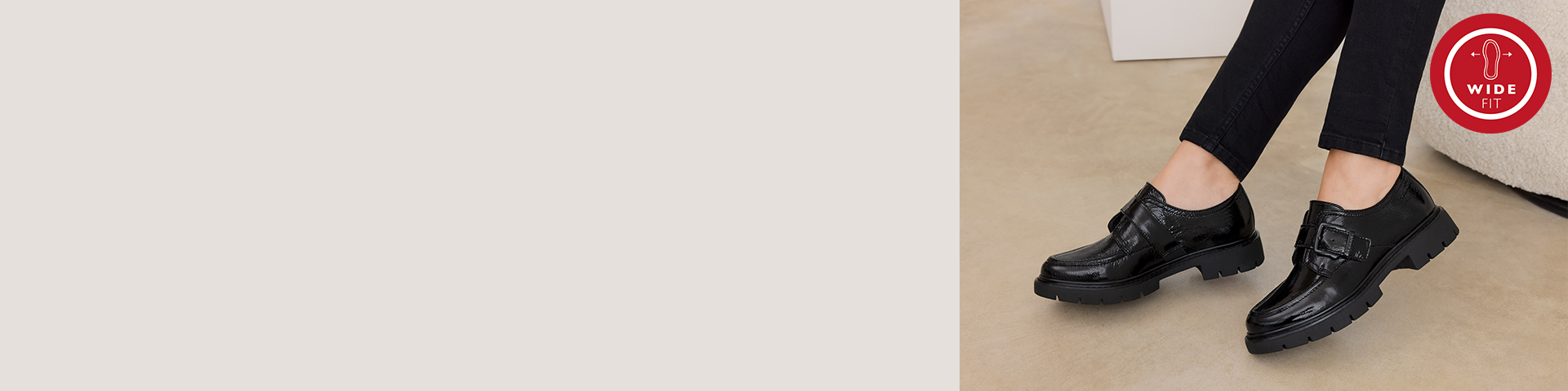 Sort l&aelig;dersko med sp&aelig;nde og robust s&aring;l, b&aring;ret til sorte bukser p&aring; beige baggrund med r&oslash;dt Wide-Fit logo &oslash;verst til h&oslash;jre.