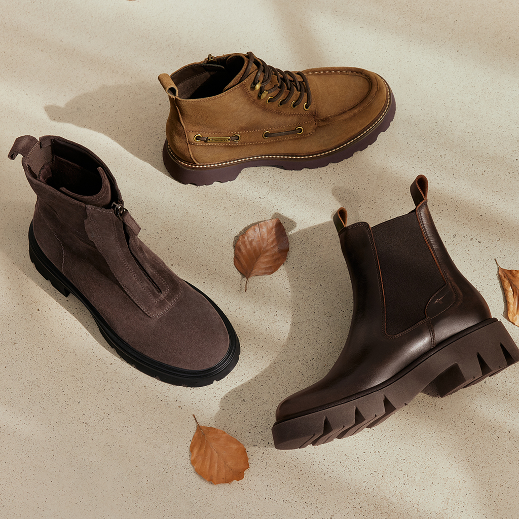Drei Herbststiefeletten in Braun und Grau auf hellem Untergrund mit Herbstbl&auml;ttern.