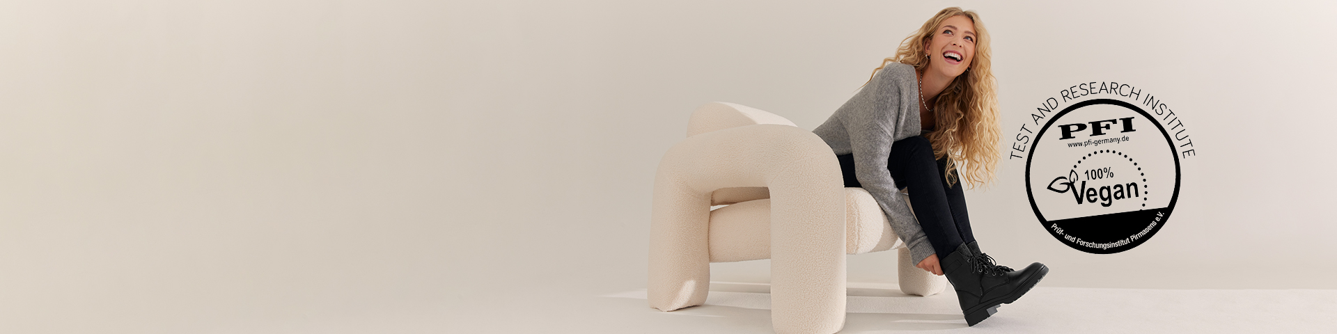 Una persona sorridente in maglione grigio e pantaloni neri si appoggia accanto a un sigillo di certificazione vegana PFI.