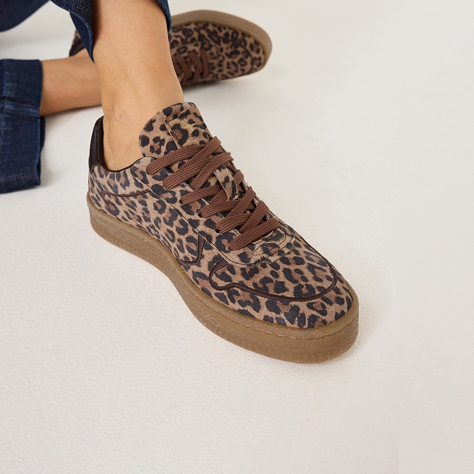 Stylischer Sneaker mit Leopardenmuster, braunen Schn&uuml;rsenkeln und flacher Gummisohle an einem Fu&szlig; mit Jeans