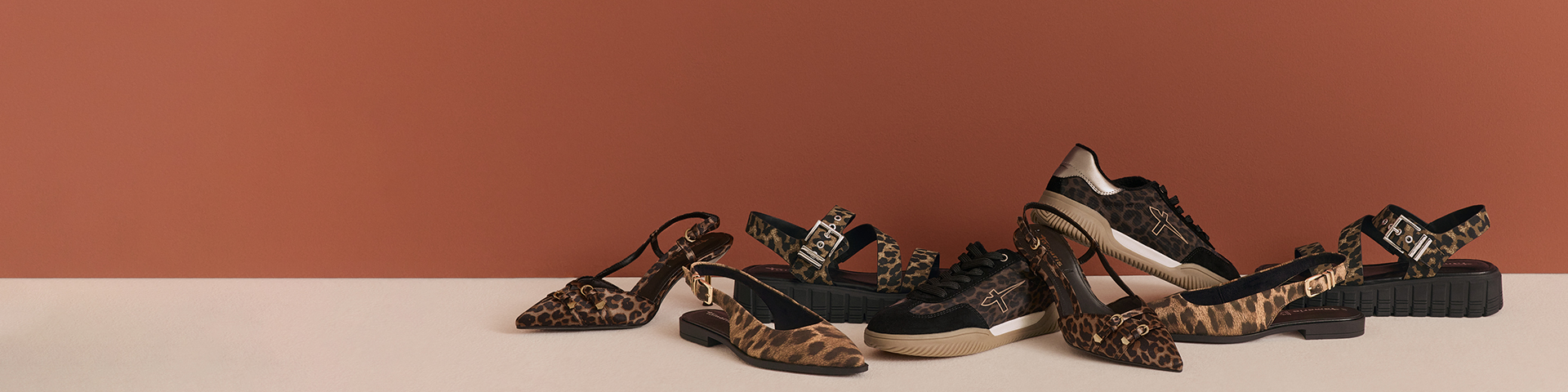 Verschiedene Damenschuhe mit Leopardenmuster in einer Reihe vor braunem Hintergrund angeordnet.