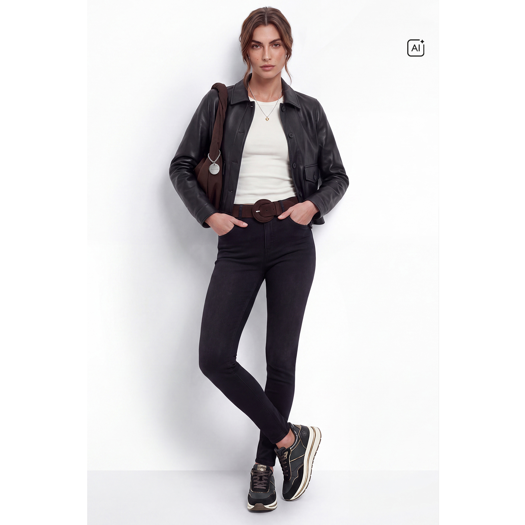 Woman in a black leather jacket, white top, black skinny jeans and trainers, with a brown bag over her shoulder.